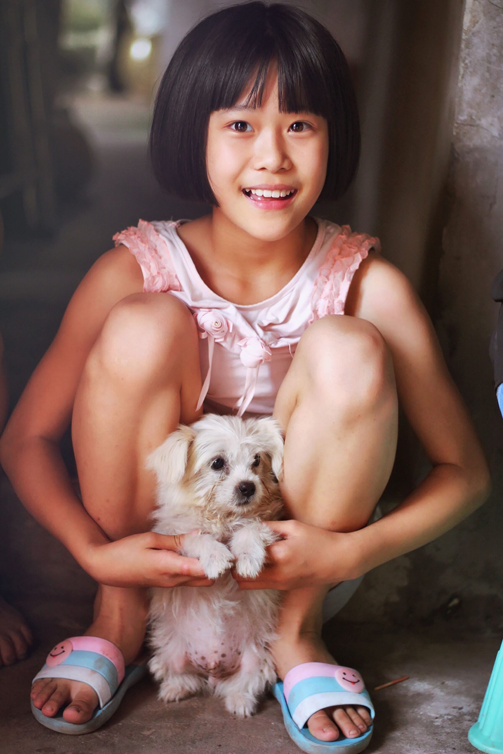 Smiling girl with cute puppy sitting indoors, showcasing joy and companionship.